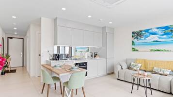 A modern kitchen with white cabinets, a dining table with chairs, a sofa, and a small coffee table.
