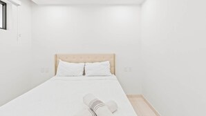 A minimalist bedroom with a bed, two pillows, a headboard, and a window. - D416 – Relaxing apartment with Balcony (Sint Maarten)