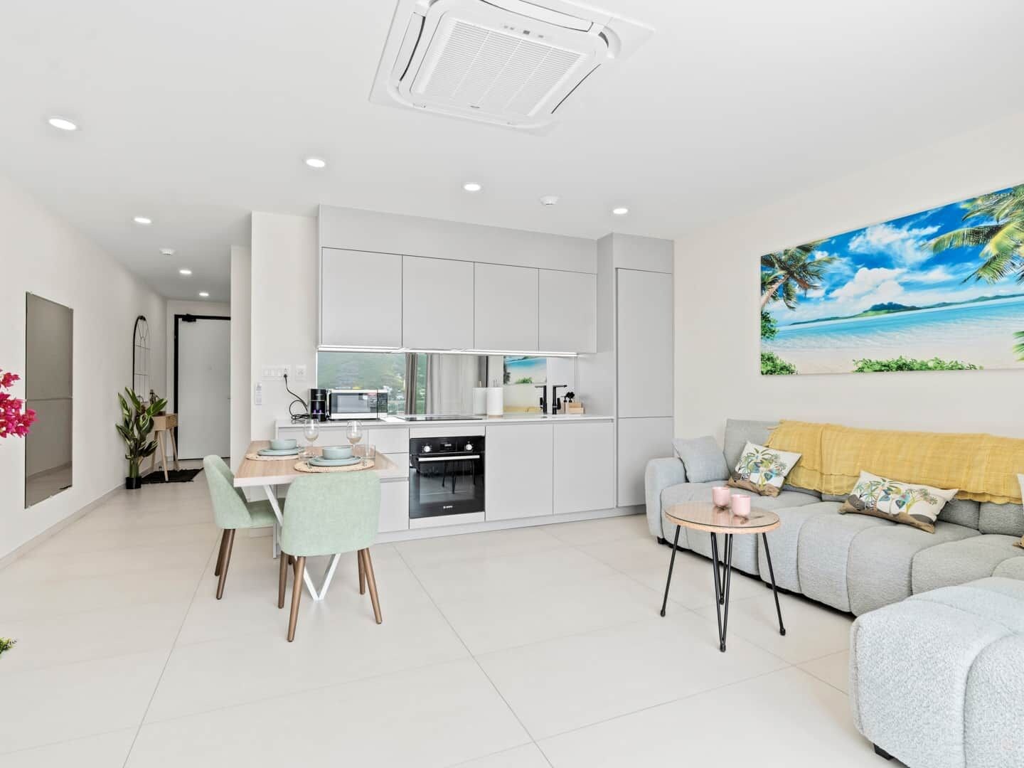A modern kitchen with white cabinets, a dining area with a table and chairs, and a living area with a sofa and a coffee table.