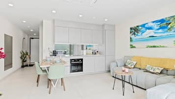 A modern kitchen with white cabinets, a dining area with a table and chairs, and a living area with a sofa and a coffee table.