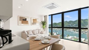Eine moderne Küche mit Essbereich, ein großes Fenster mit Blick auf einen Yachthafen und Hügel sowie ein Deckenlüfter.