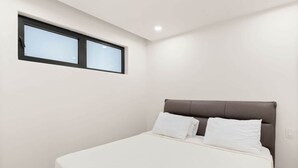 Ein Schlafzimmer mit Bett, Fenster und Lichtschalter an der Wand.