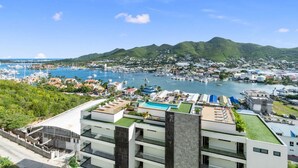 Ein Hotel an der Küste mit einem Dachpool, einem Yachthafen im Hintergrund und üppigen, grünen Hügeln.