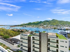 A modern building with a rooftop pool, a marina with boats, and a mountainous backdrop. - C335 – Comfortable Lagoon View Apartment (Sint Maarten)