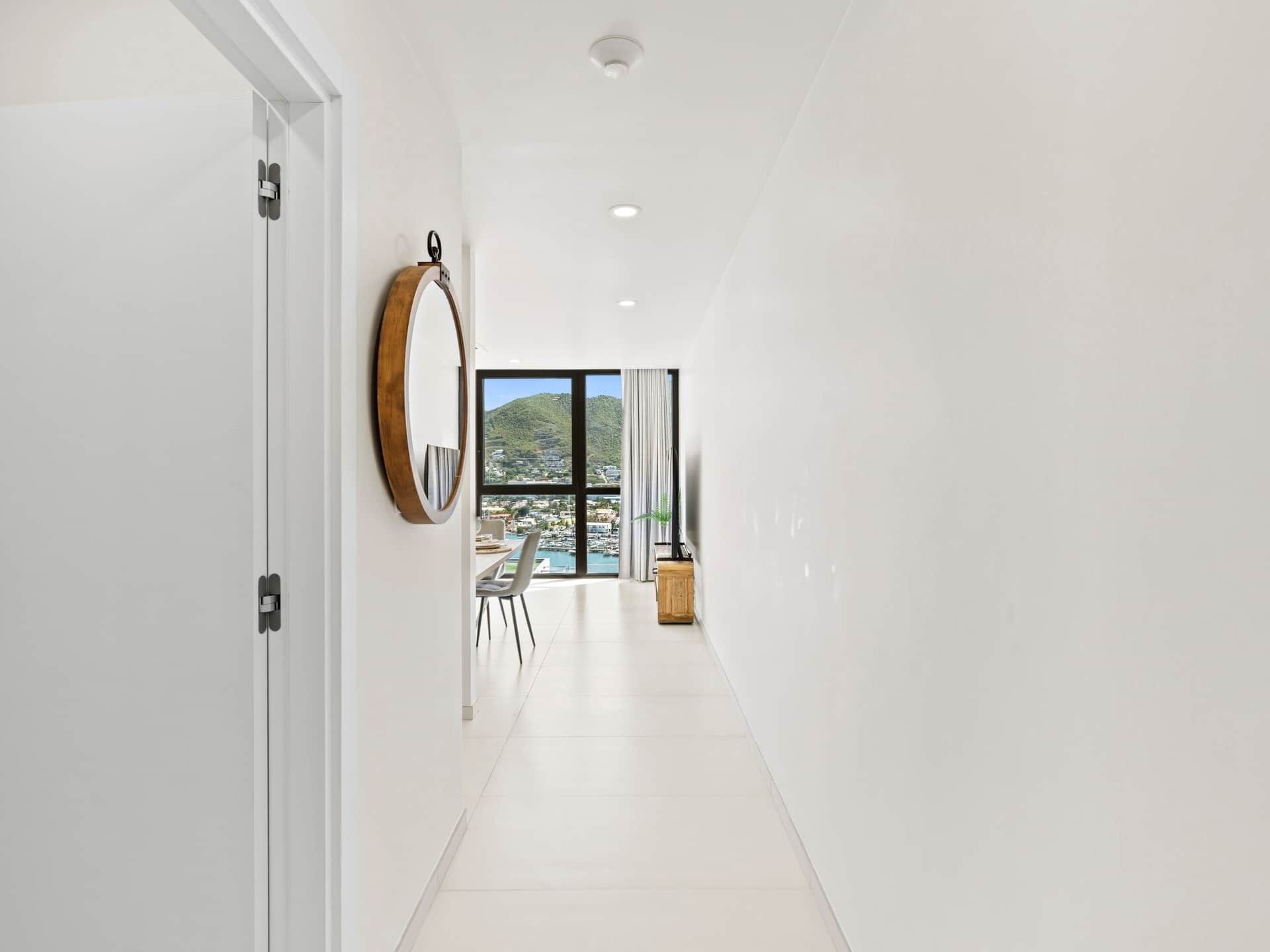 A hallway with a view of a marina and hills, a round mirror, and a dining area with chairs and a table.