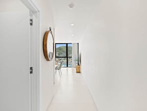 A hallway with a view of a marina and hills, a round mirror, and a dining area with chairs and a table. - C335 – Comfortable Lagoon View Apartment (Sint Maarten)