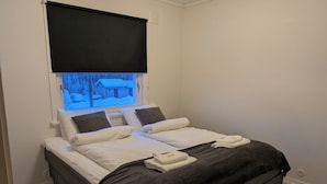 Ein Einzelbett mit weißer Bettwäsche, zwei Kissen, einer dunkelgrauen Decke und einem zusammengelegten Handtuch daneben.
