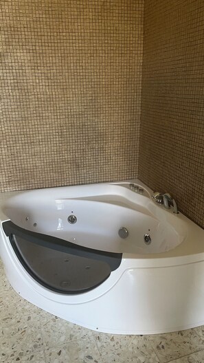 Une baignoire blanche aux bords incurvés, dotée d’un siège intégré et d’un panneau de commande avec plusieurs boutons. Les murs sont recouverts de carreaux formant un petit motif carré.