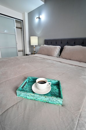Un lit bien fait, avec un plateau sur lequel se trouvent une tasse de café, une lampe de chevet et une tête de lit agrémentée d’oreillers.
