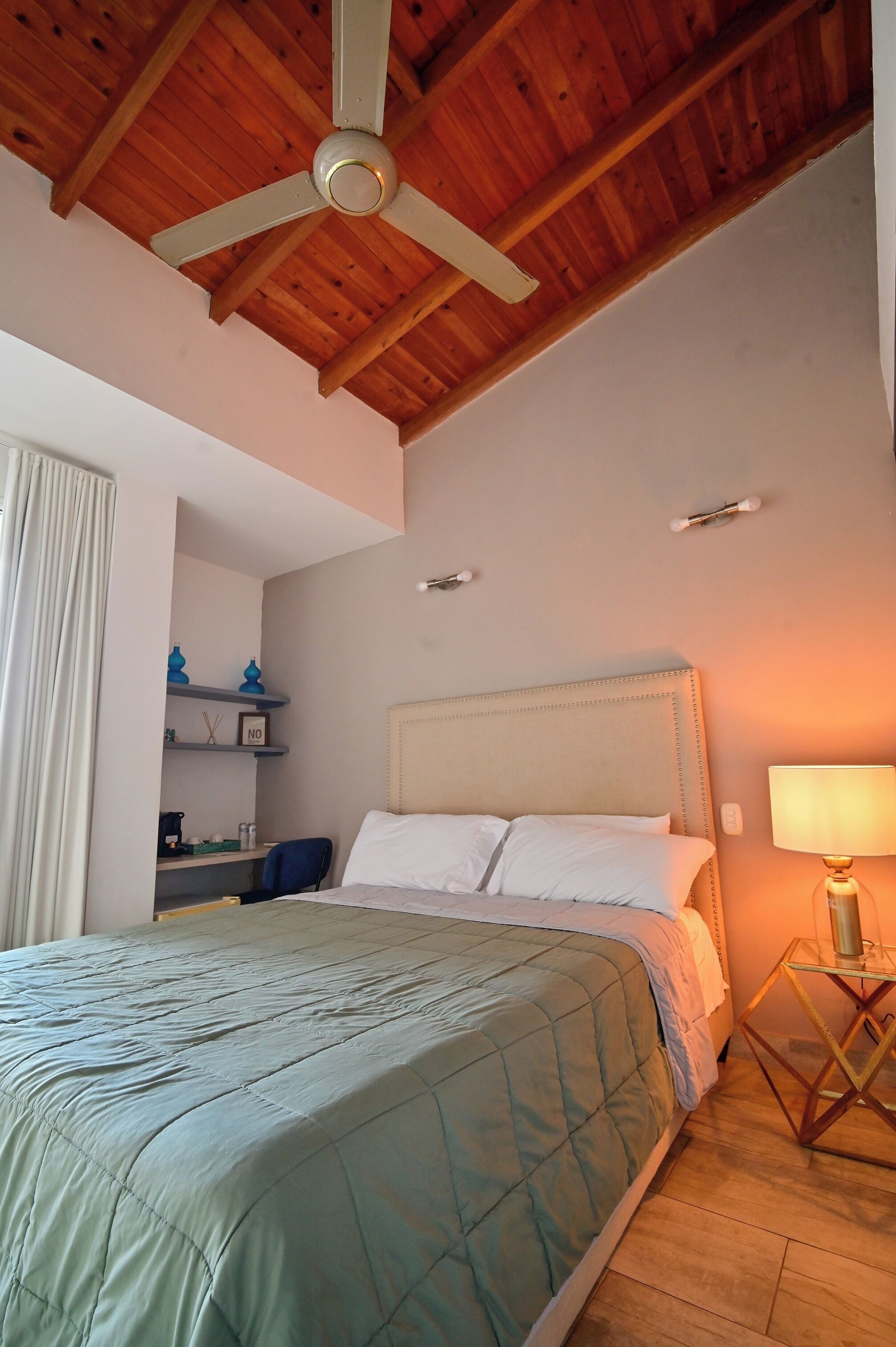 A bedroom with a bed, a ceiling fan, a bedside lamp, and a desk with a chair.