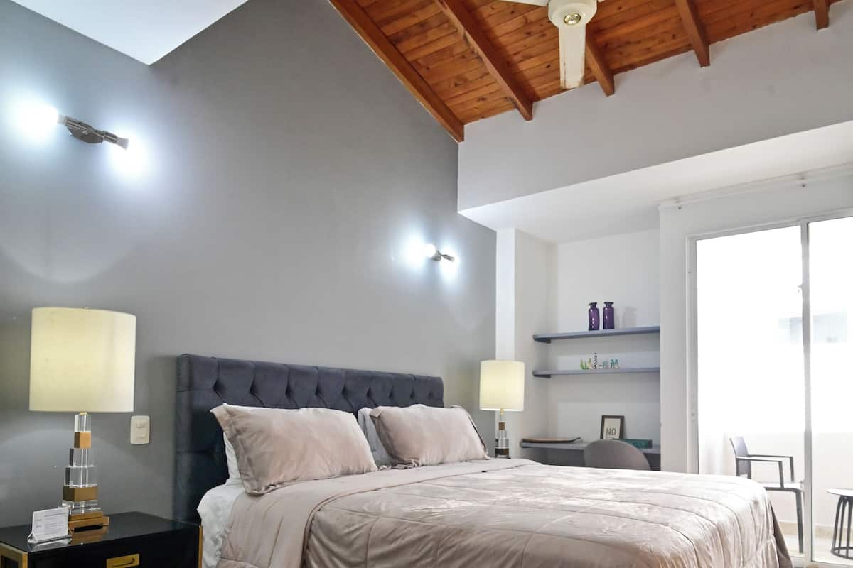 A bedroom with a bed, bedside tables, a ceiling fan, and a desk with a chair.