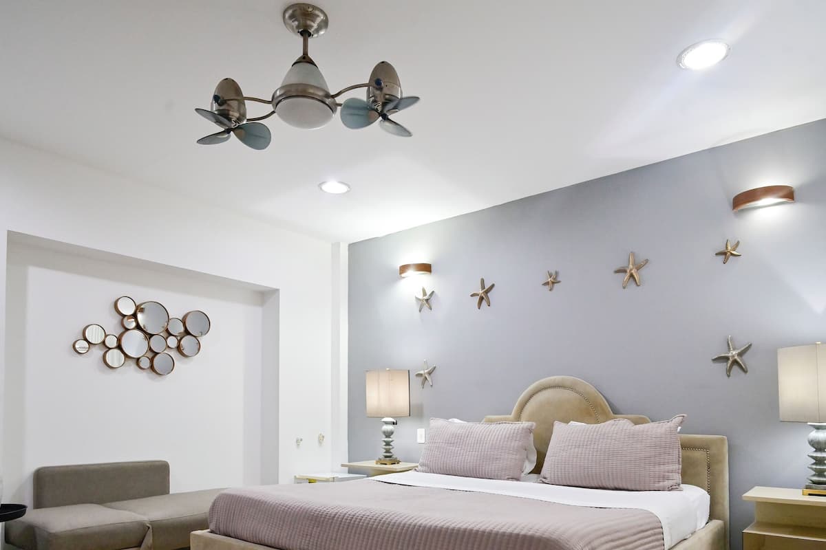 A bedroom with a bed, a sofa, a ceiling fan, and wall decorations.