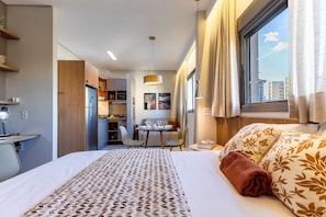 Habitación de hotel con cama, escritorio, silla, mesa de comedor y vista a la ciudad por la ventana.