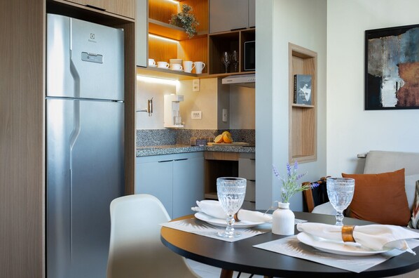 Una cocina moderna con un refrigerador empotrado, una mesa de comedor con platos y vasos, y una planta pequeña en la encimera.