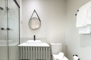 A modern bathroom with a glass shower enclosure, a white sink, a toilet, and a hanging mirror. - AD330 - 1002 (São Paulo)