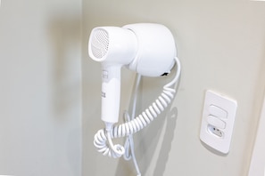 Un secador de pelo blanco montado en la pared, cerca un enchufe.