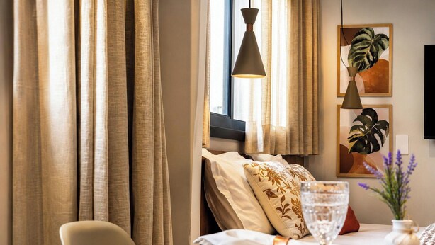 Um quarto com uma cama, uma mesa e um copo de água, além de cortinas.