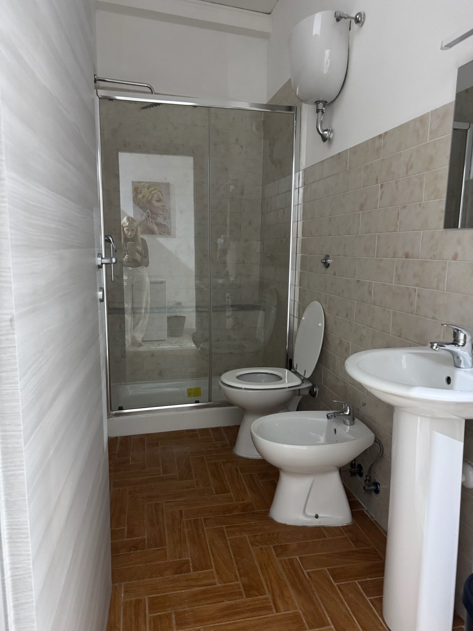 A bathroom with a glass-enclosed shower, two toilets, and a pedestal sink.