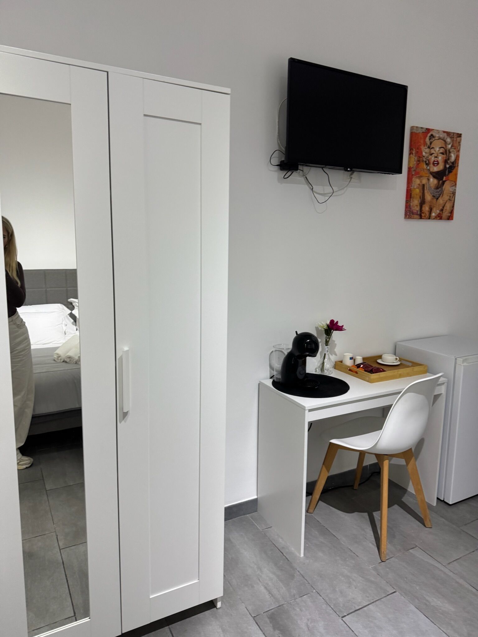 A modern room with a white wardrobe, a desk with a chair, a flat-screen TV, and a painting on the wall.