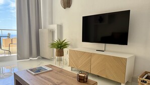 Un salon moderne doté d’un téléviseur à écran plat, de meubles en bois, d’une plante en pot et offrant une vue sur l’extérieur.