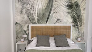 Une chambre avec un grand lit, du linge de lit blanc, deux tables de chevet et un mur orné d’un motif de feuilles.