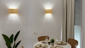 Un espace repas comprenant une table ronde, des chaises blanches et deux appliques murales.