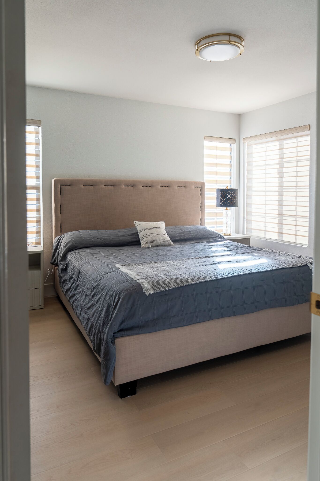 Un dormitorio con cama, mesita de noche, lámpara y ventana con persianas.