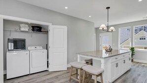 Une cuisine moderne dotée d’un lave-linge et d’un sèche-linge intégrés, d’un îlot central avec un comptoir en granit et des tabourets de bar, et offrant une vue sur le quartier grâce à de grandes fenêtres.