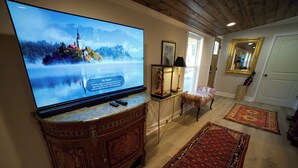 A living room with a large flat-screen TV on a marble console, a wooden cabinet, a small table with a lamp, a chair, and a red patterned rug. - Spacious Beautiful Unique place to stay in Morganton, NC. (Morganton)