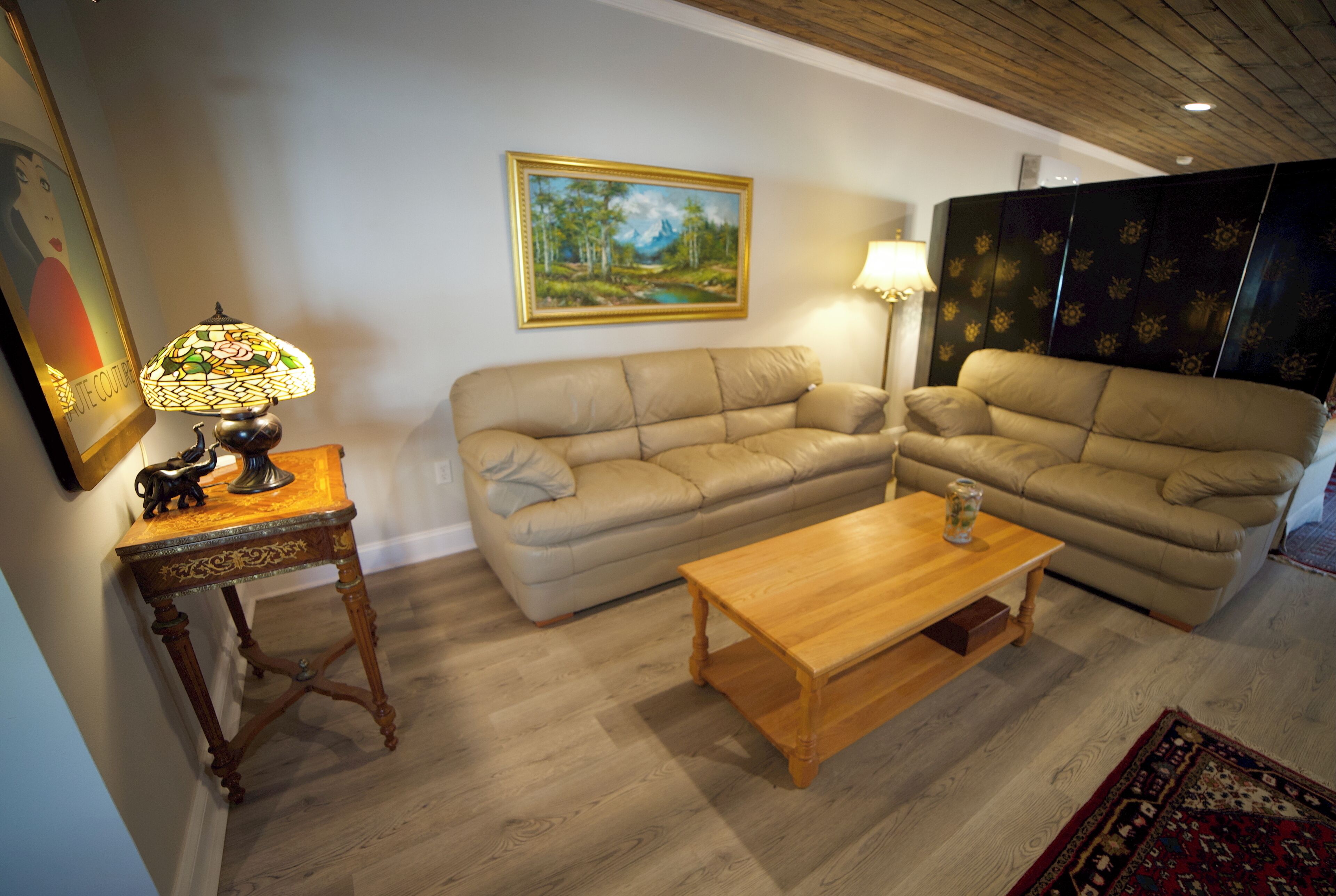 A living room with a beige sofa, a wooden coffee table, a lamp, and a painting on the wall.