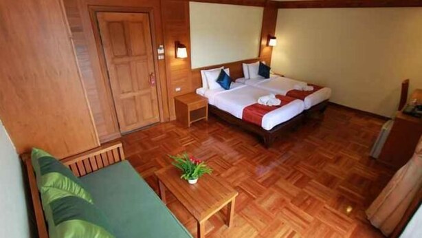 Una camera d'albergo con pavimento in legno, un letto con lenzuola bianche, un divano verde e un tavolino con una pianta.