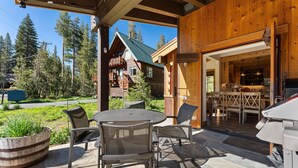 A wooden cabin with a patio area featuring a round table and chairs, a large planter, and a view of the surrounding forest. - A Serene Mountain Autumn/Fall Getaway (Soda Springs)
