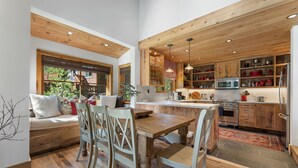 A kitchen with wooden cabinets, a dining area with a bench and chairs, and a view of the outdoors. - A Serene Mountain Autumn/Fall Getaway (Soda Springs)
