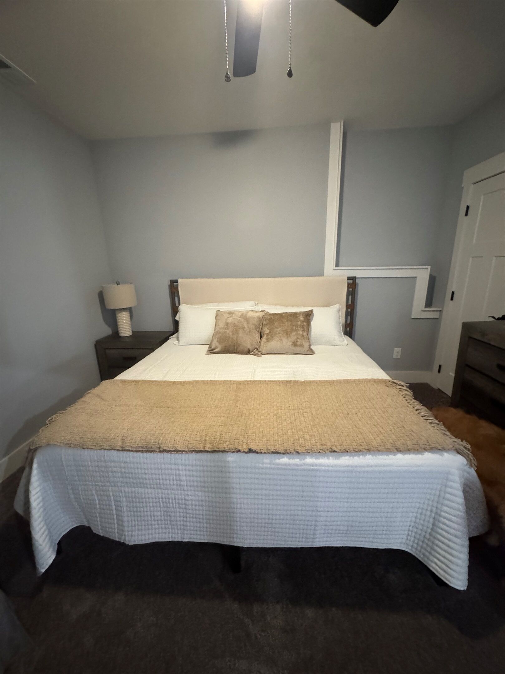 A bedroom with a bed, a nightstand, a lamp, and a wall-mounted shelf.