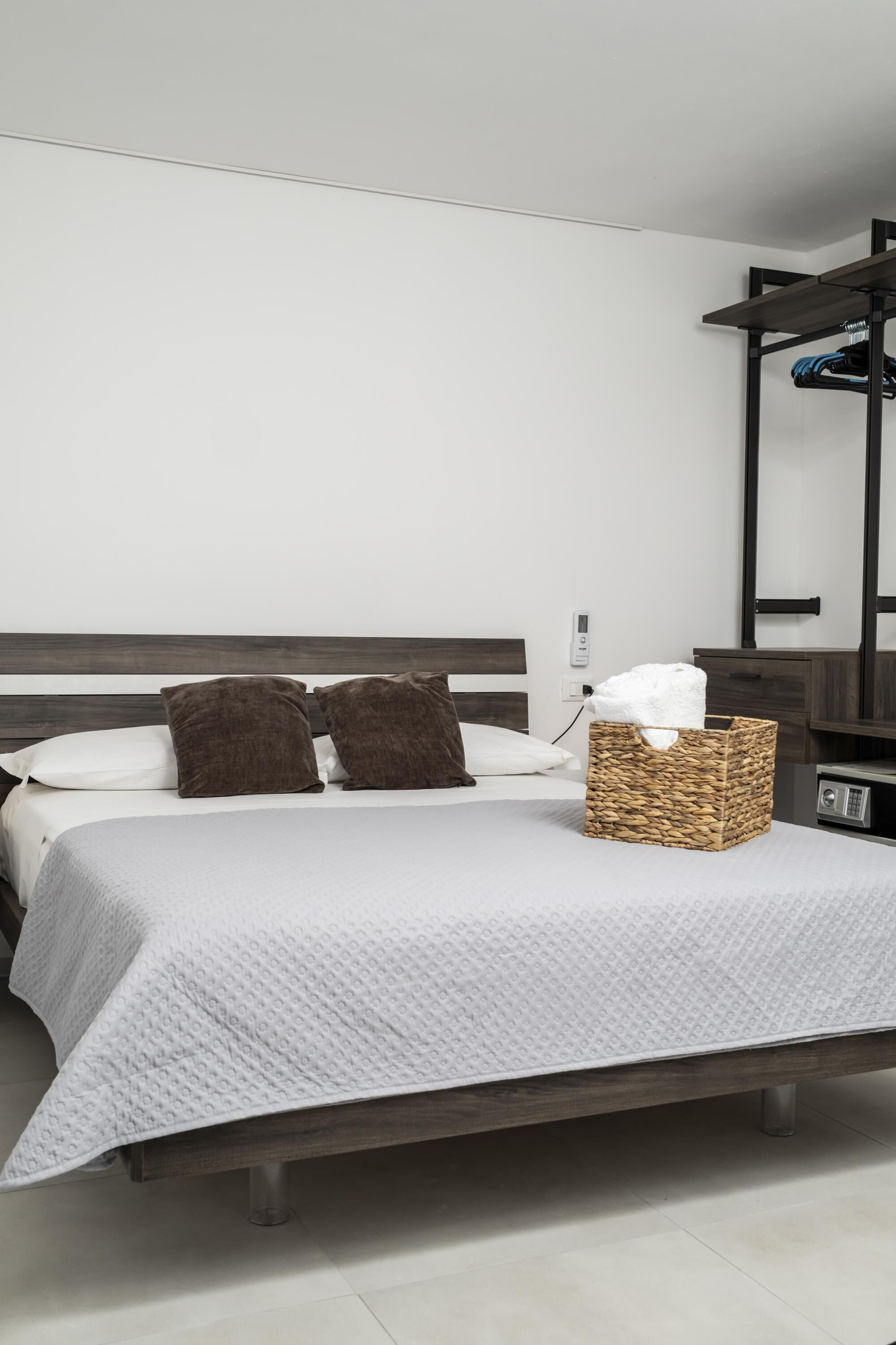 A neatly made bed with a white quilt, two brown pillows, and a wicker basket on the side.
