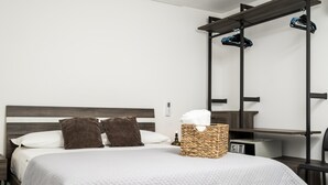 Une chambre d’hôtel moderne équipée d’un lit, d’une table de chevet, d’un petit bureau et d’un porte-serviettes fixé au mur.
