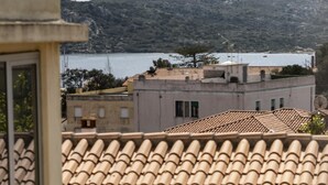 Une terrasse dotée d’un toit en tuiles, avec une table et des chaises, offrant une vue sur une étendue d’eau et un paysage montagneux.