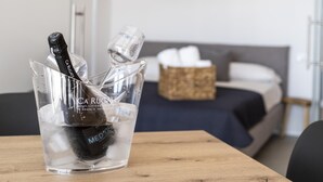 Une chambre avec un lit, une table de chevet sur laquelle se trouvent une bouteille et des verres, et une table en bois avec un plateau en verre transparent.