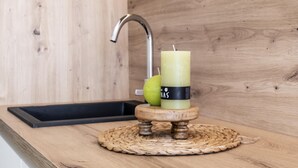 Une cuisine avec un plan de travail en bois, un évier en acier inoxydable et une bougie posée sur un sous-verre en fibres tressées.