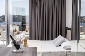 A hotel room with a bed, a glass table with a bottle, and a view of buildings and hills. - Suite Luma - La Maddalena (La maddalena)