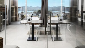 Un espace repas moderne avec une cloison en verre, une table avec des chaises et une vue sur les montagnes et l’eau.