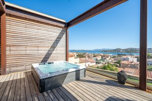 En træterrasse med et boblebad og udsigt over en kystby.