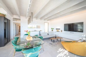 A modern living room with a glass coffee table, teal chairs, a sofa, and a flat-screen TV mounted on the wall. - Attico Salia - La Maddalena (La maddalena)