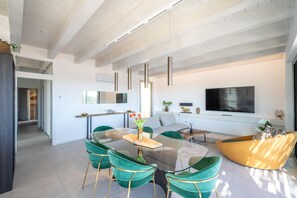 Ein modernes Wohnzimmer mit einem Glastisch, grünen Stühlen, einer Couch und einem wandmontierten Flachbildfernseher.