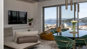 A modern living room with a sofa, a green chair, a glass table, and a view of the sea. - Attico Salia - La Maddalena (La maddalena)