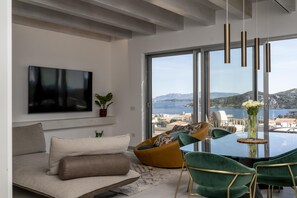 Ein modernes Wohnzimmer mit einer Couch, einem grünen Sessel, einem Glastisch und Meerblick.