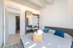 A modern bedroom with a large bed, a bedside table, a mirror, and a hanging light fixture. - Attico Salia - La Maddalena (La maddalena)
