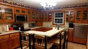 Una cocina con armarios de madera, microondas, tostadora, refrigerador y un comedor con sillas de madera.