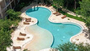 Una piscina con diseño ondulado, rodeada de tumbonas y una zona de arena.