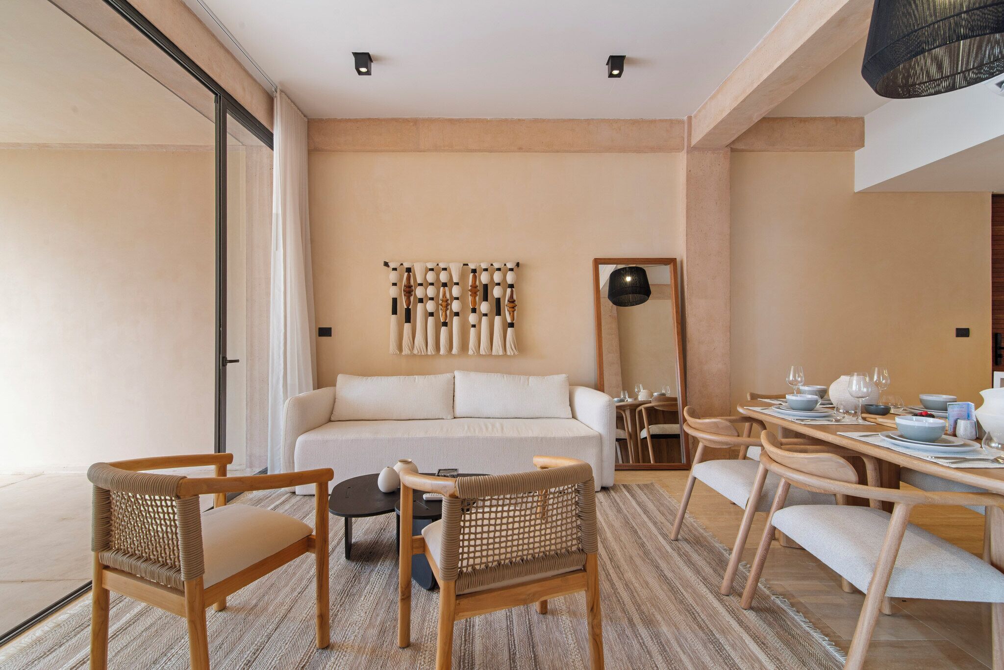 A modern hotel room with a sofa, two wooden chairs, a dining table set for four, and a large mirror.